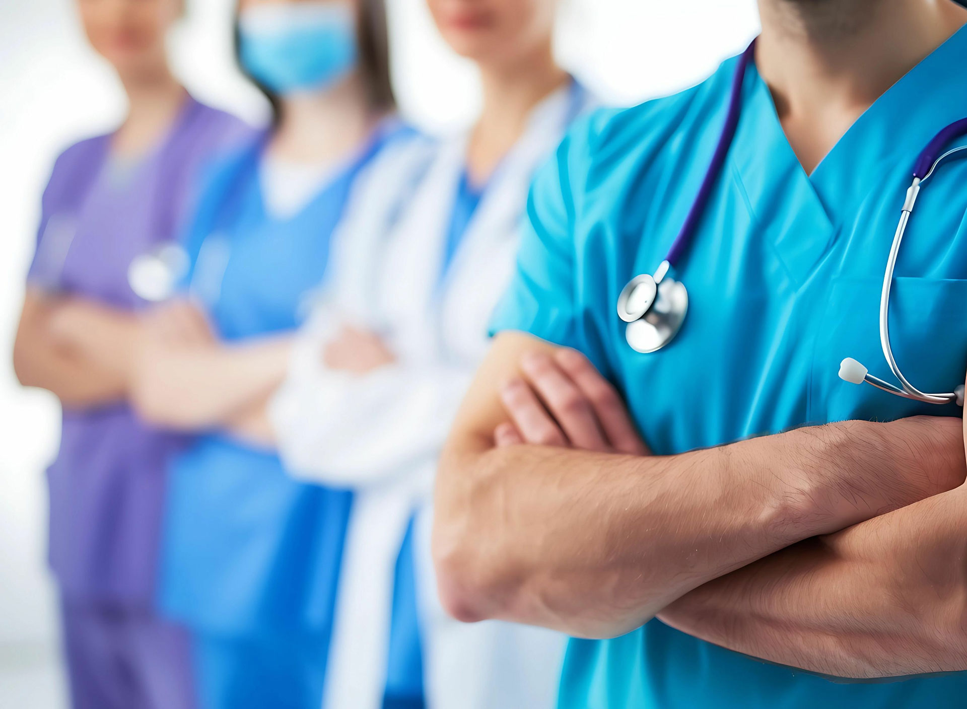 A group of five healthcare professionals, each wearing a different colored scrub and stethoscope, standing in front of a white background.