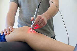 The image shows a person performing a medical procedure on another individual s leg, using a device that appears to be an ultrasound machine.