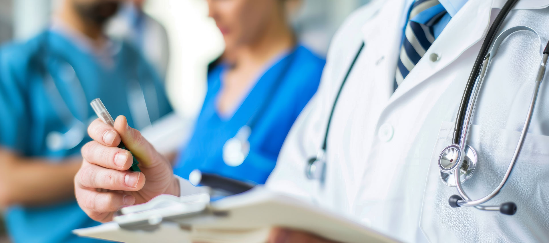 Medical professionals at a table, one writing in a clipboard, surrounded by healthcare-related items.