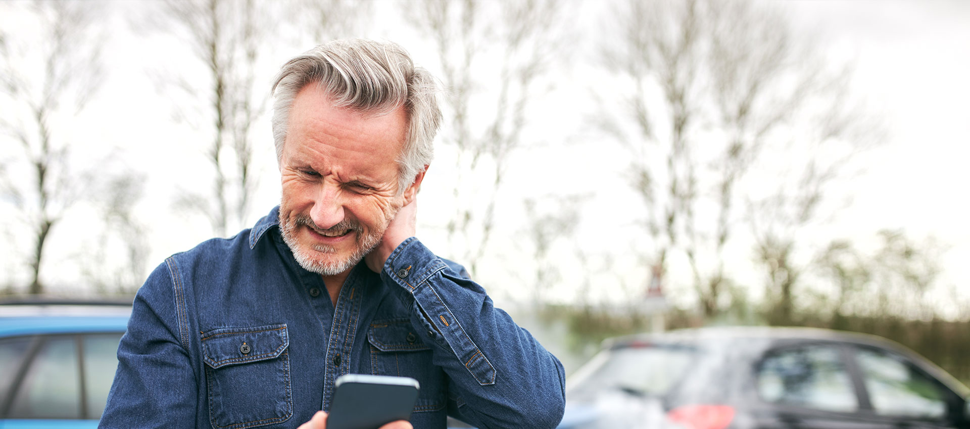 A man in a blue denim shirt using a smartphone while standing outdoors.