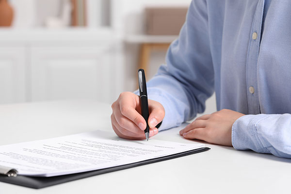 The image shows a person signing a document with a pen.