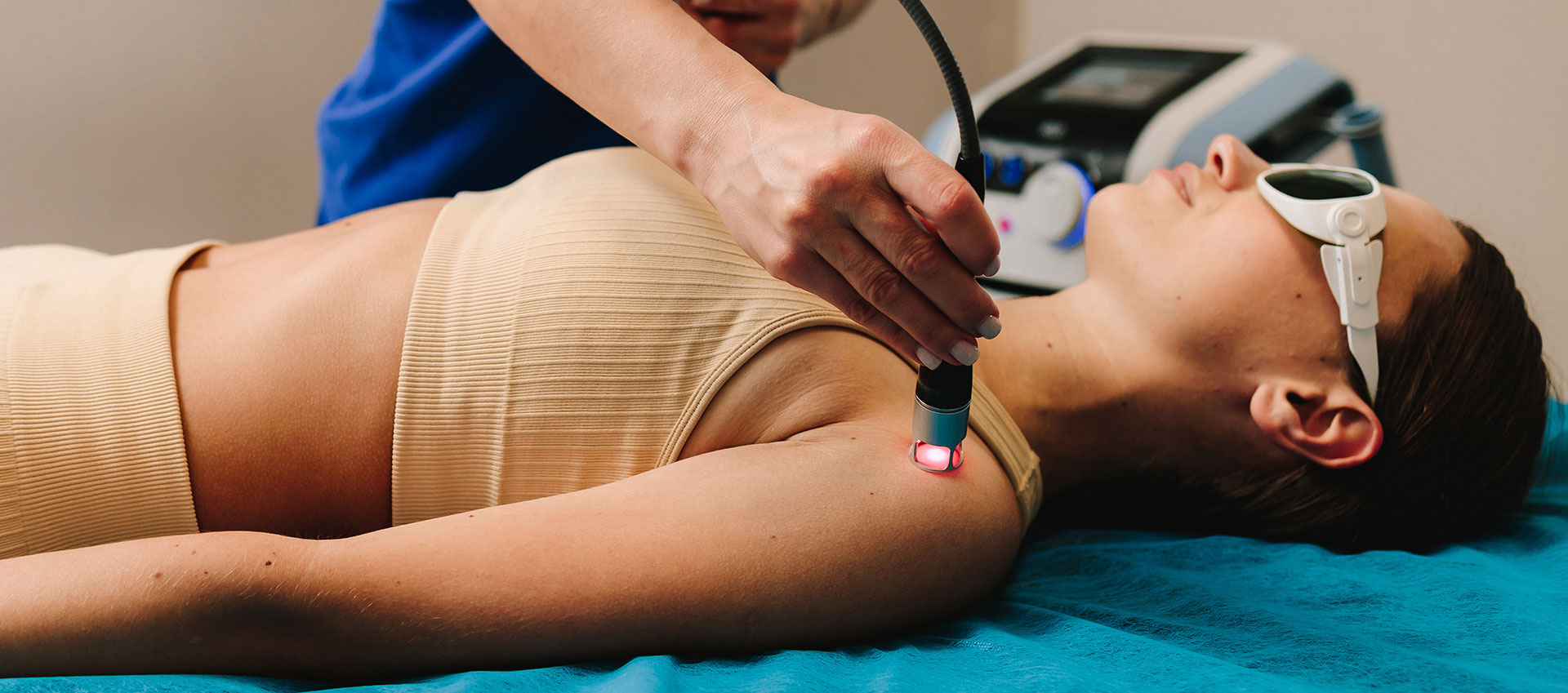 A woman lying on a massage table receiving treatment, with a practitioner using a device to apply pressure or heat.