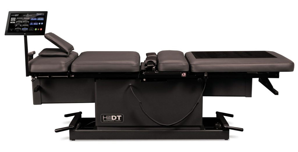 A modern, black and silver medical examination table with adjustable components, positioned against a plain background.