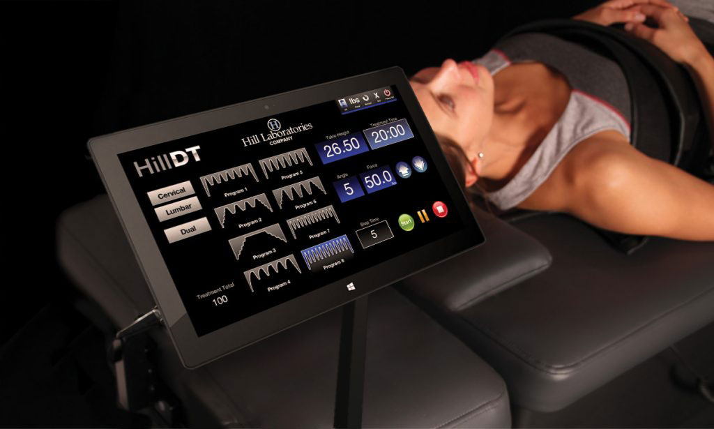 The image shows a person lying on a massage table with a digital tablet displaying various massage options and settings.