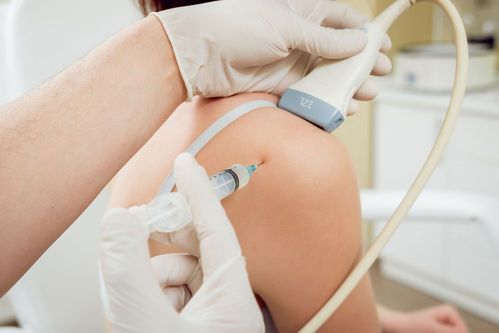 The image depicts a medical professional administering an injection to the back of a seated individual, with the person wearing a white gown and having their skin punctured by a needle.