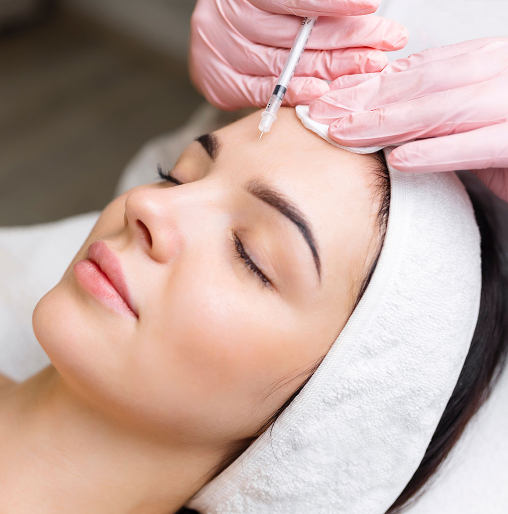 A woman receiving a beauty treatment at a salon, with a professional applying a mask to her face.